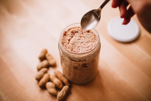 pexels photo 23384624 23384624 1 A glass jar of homemade peanut butter on a wooden table with peanuts and a spoon.